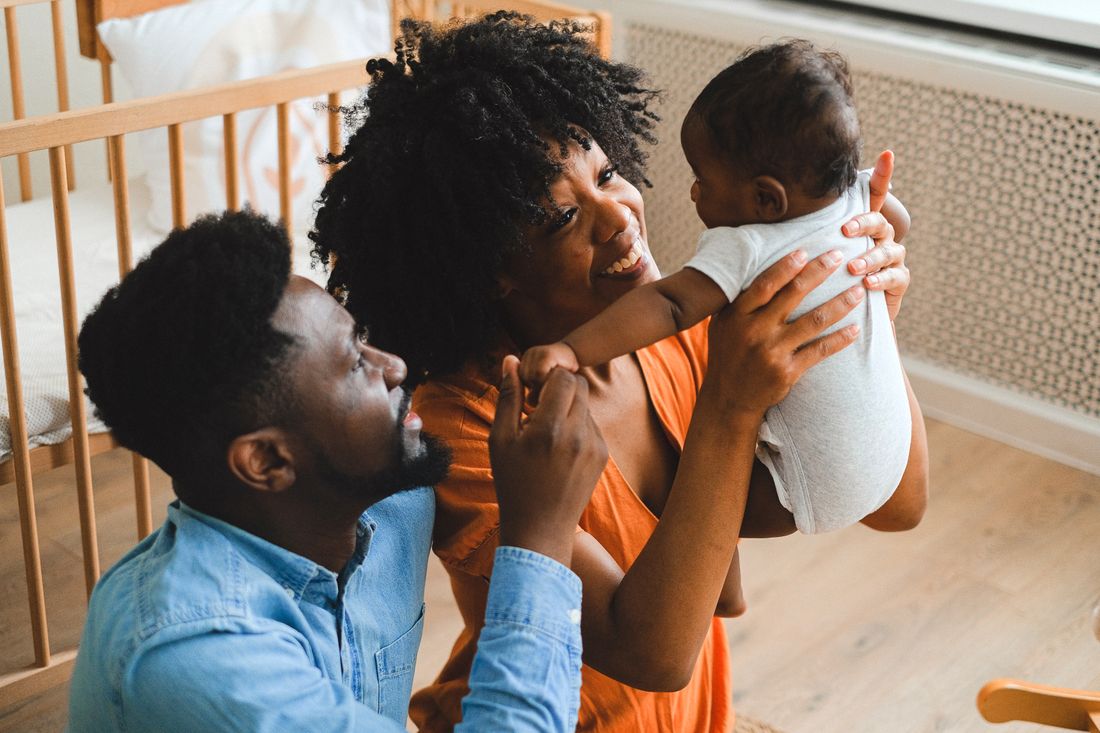 Two parents smile at their baby, held between them at home