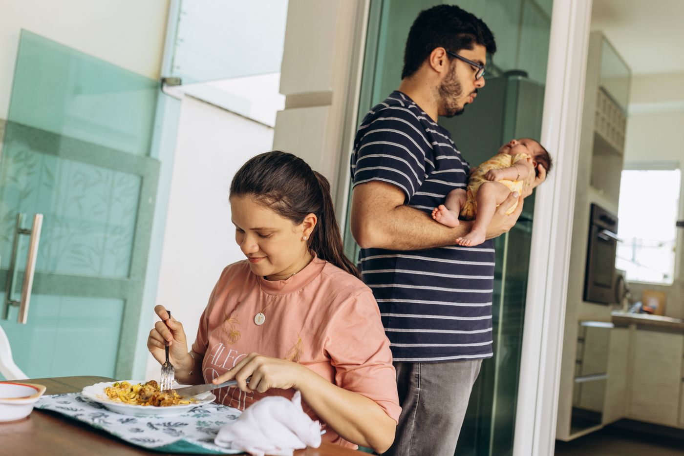 A dad holds the baby so the mother can eat her meal