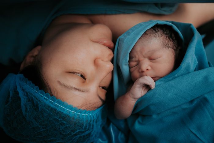A mother holds her newborn wrapped in a blue hospital blanket