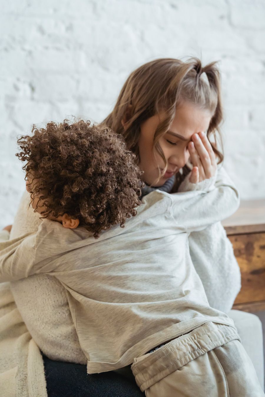 A tired mother rests her hand on her head while hugging her son