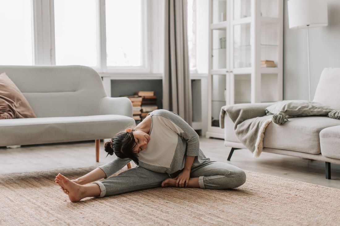 A woman stretches in a relaxed yoga pose on a rug at home