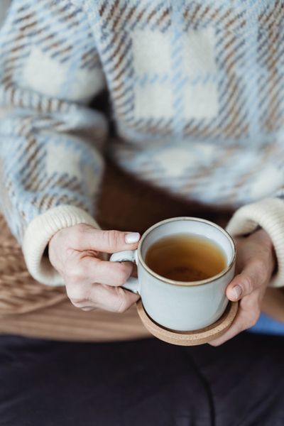 A woman in a warm sweater holds a cup of tea