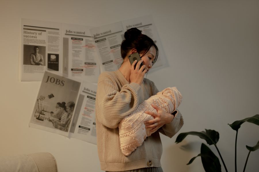 An Asian mother holds her newborn in one arm while taking a phone call